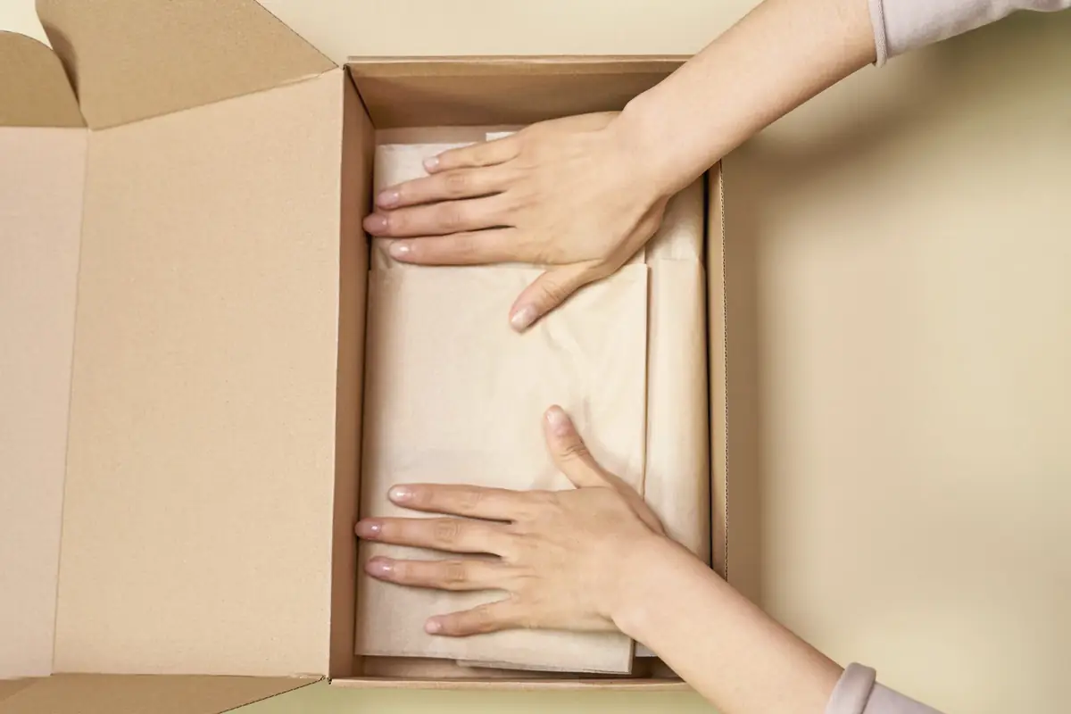 Manos preparando un pedido en una caja de cartón con papel de seda