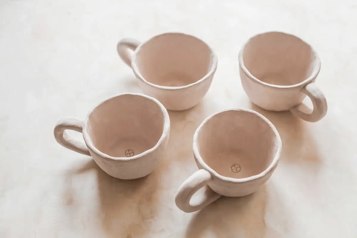 Cuatro tazas de cerámica rosa pálido hechas a mano sobre una superficie blanca
